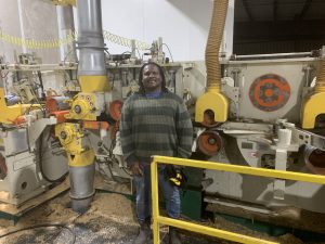 Un homme se tient devant une raboteuse Gilbert flambant neuve. Des copeaux de bois et du brin de scie jonchent le sol, témoins de l'activité intense qui règne dans cet espace dédié à la transformation du bois. La raboteuse Gilbert, imposante et robuste, semble prête à relever tous les défis, prête à transformer les pièces de bois brut.