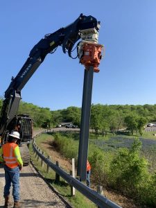 On the side of a road, a specialized team is installing sheet piles using a powerful machine, the MG-60 Gilbert. Two experts are overseeing the smooth running of the operations and the safety of everyone.
